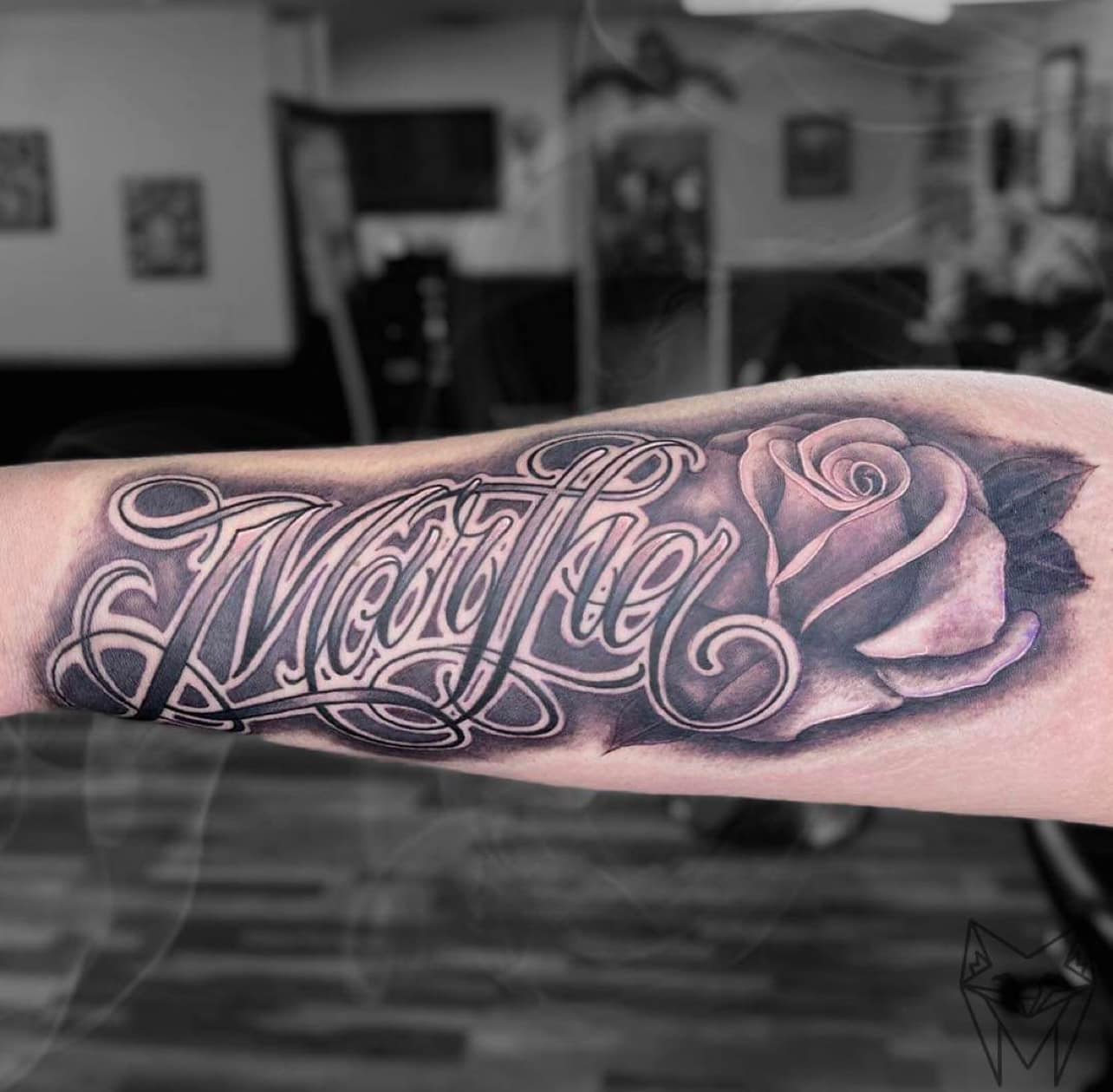 Custom script tattoo reading Martha beside a black and grey rose, on a forearm