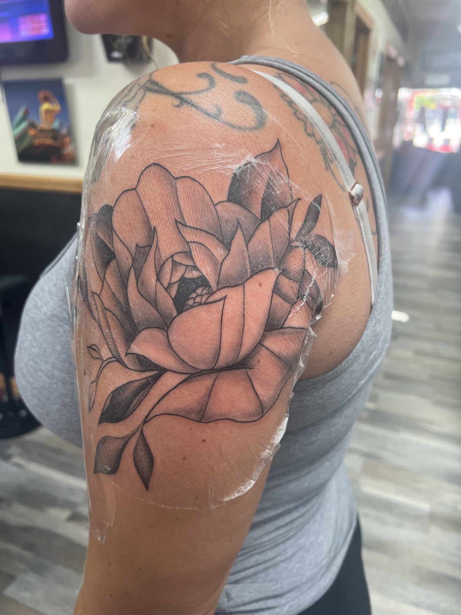 Freshly wrapped black and grey peony floral tattoo on a shoulder