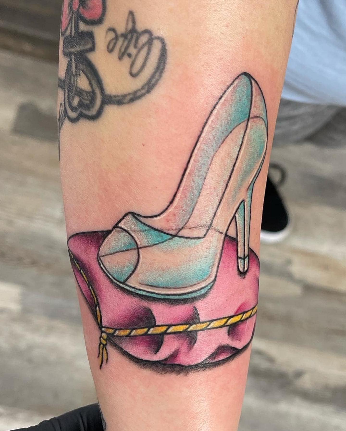 Color tattoo of a glass high-heel slipper on a pink pillow, on a forearm